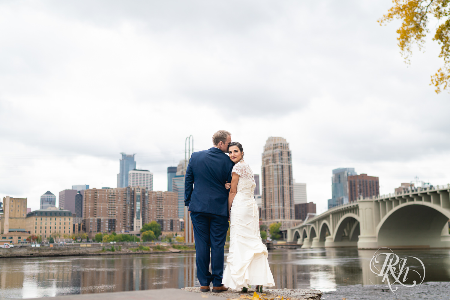 Bride and groom smile in front of the Minneapolis skyline.