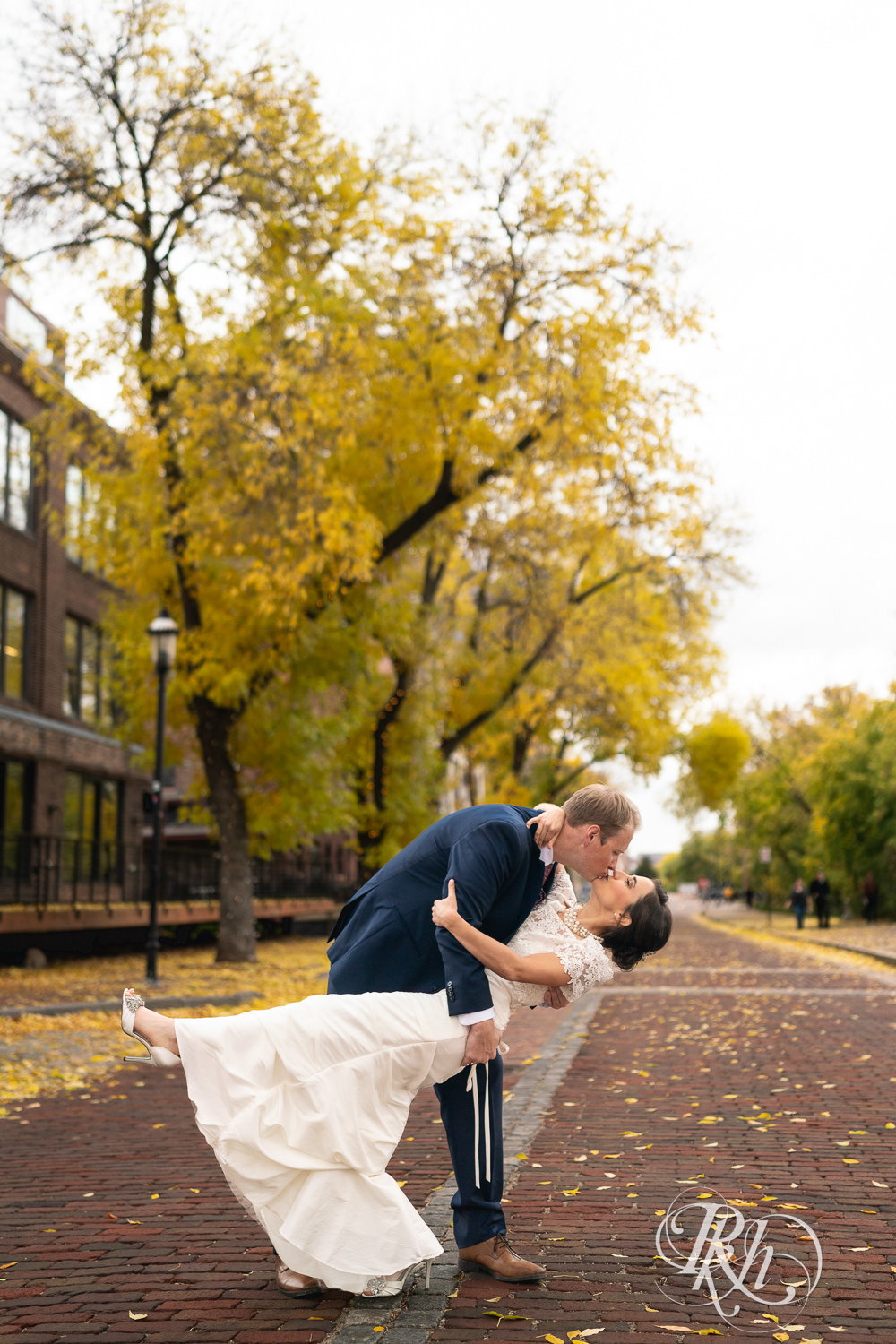 Bride and groom dip and kiss on cobblestone in Saint Anthony Main in Minneapolis, Minnesota.