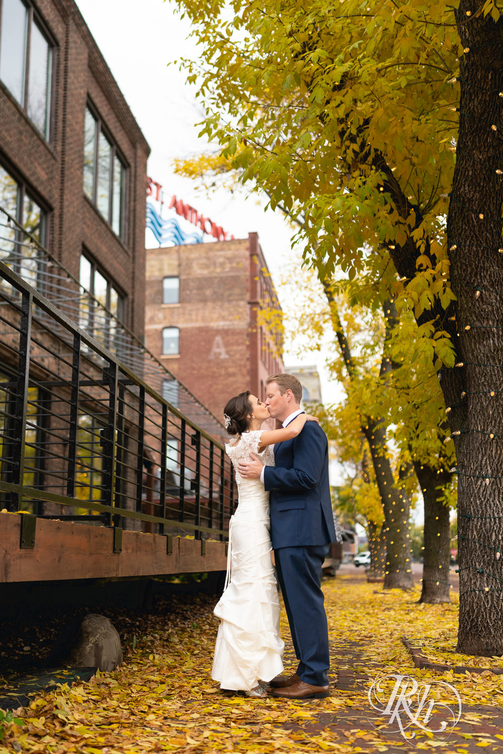 Bride and groom kiss in fall leaves in Saint Anthony Main in Minneapolis, Minnesota.