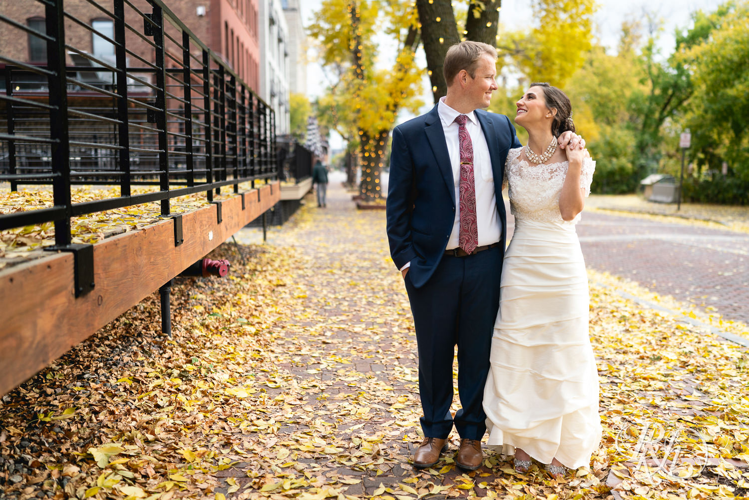 Bride and groom smile in fall leaves in Saint Anthony Main in Minneapolis, Minnesota.