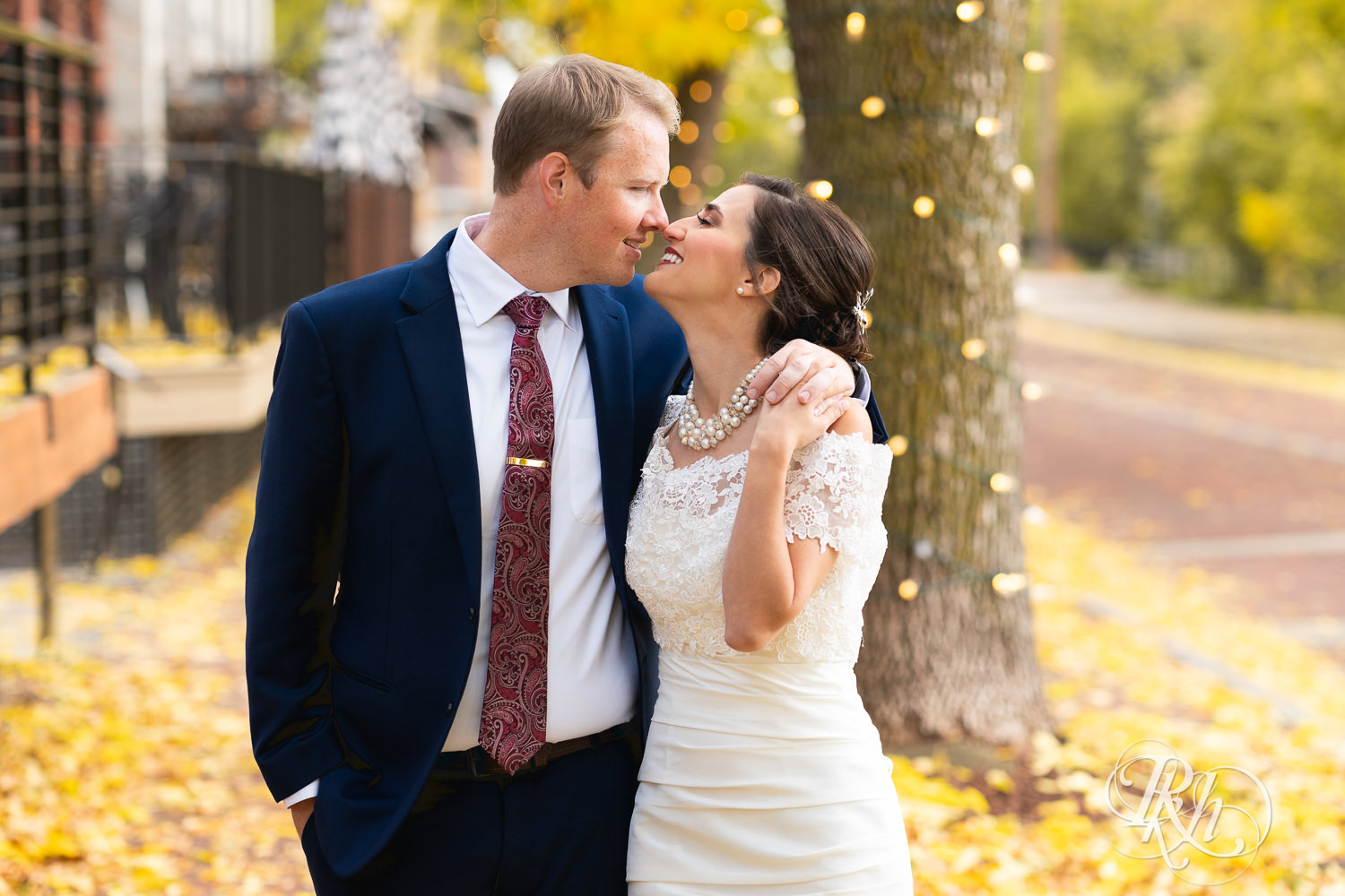 Bride and groom smile in fall leaves in Saint Anthony Main in Minneapolis, Minnesota.