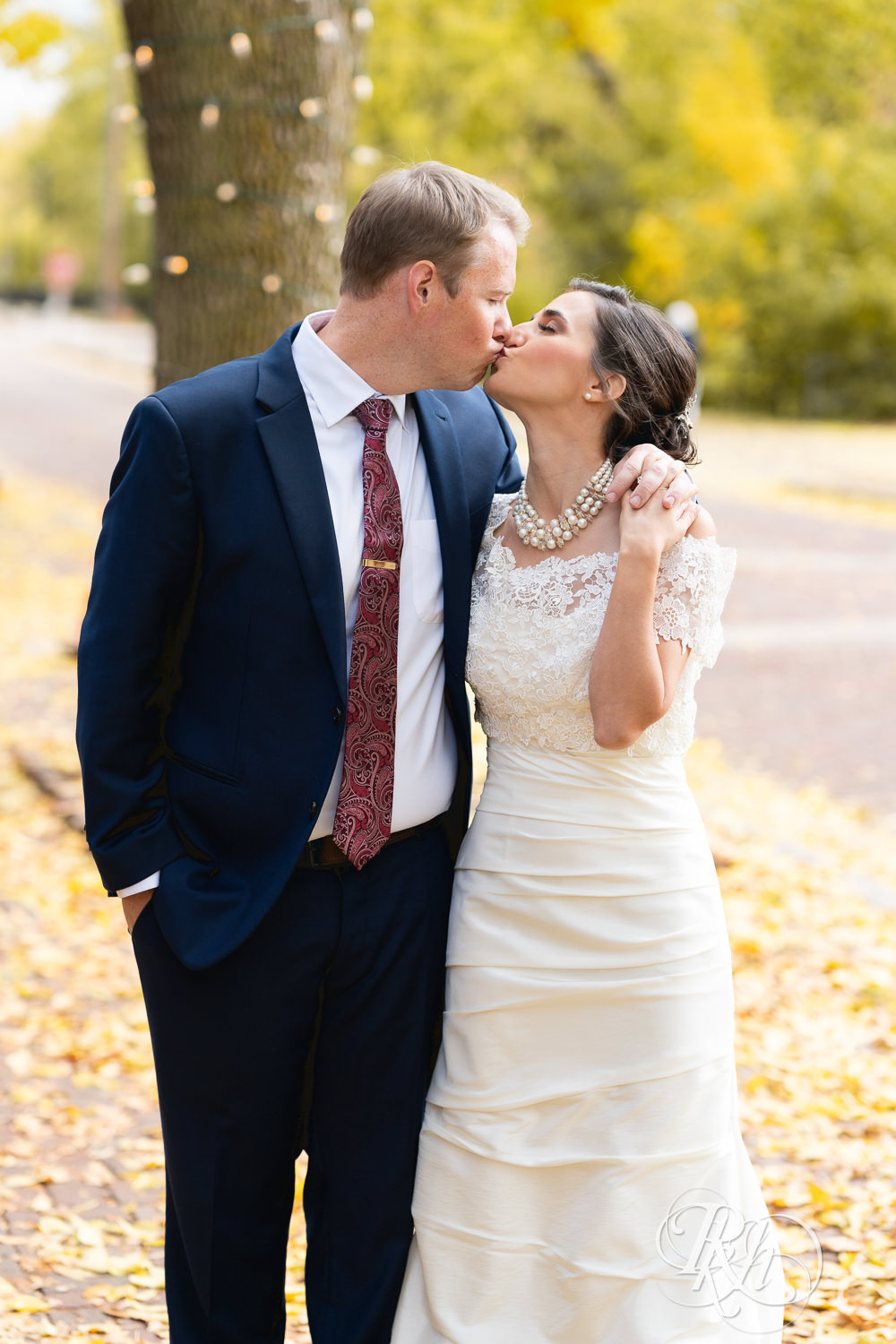 Bride and groom kiss in fall leaves in Saint Anthony Main in Minneapolis, Minnesota.