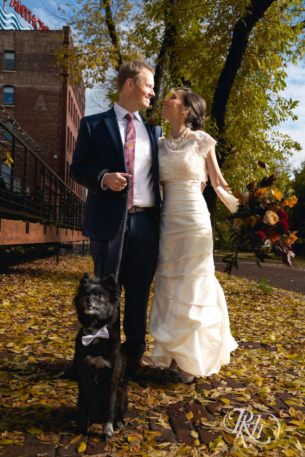 Bride and groom smile with their dog in Saint Anthony Main in Minneapolis, Minnesota.