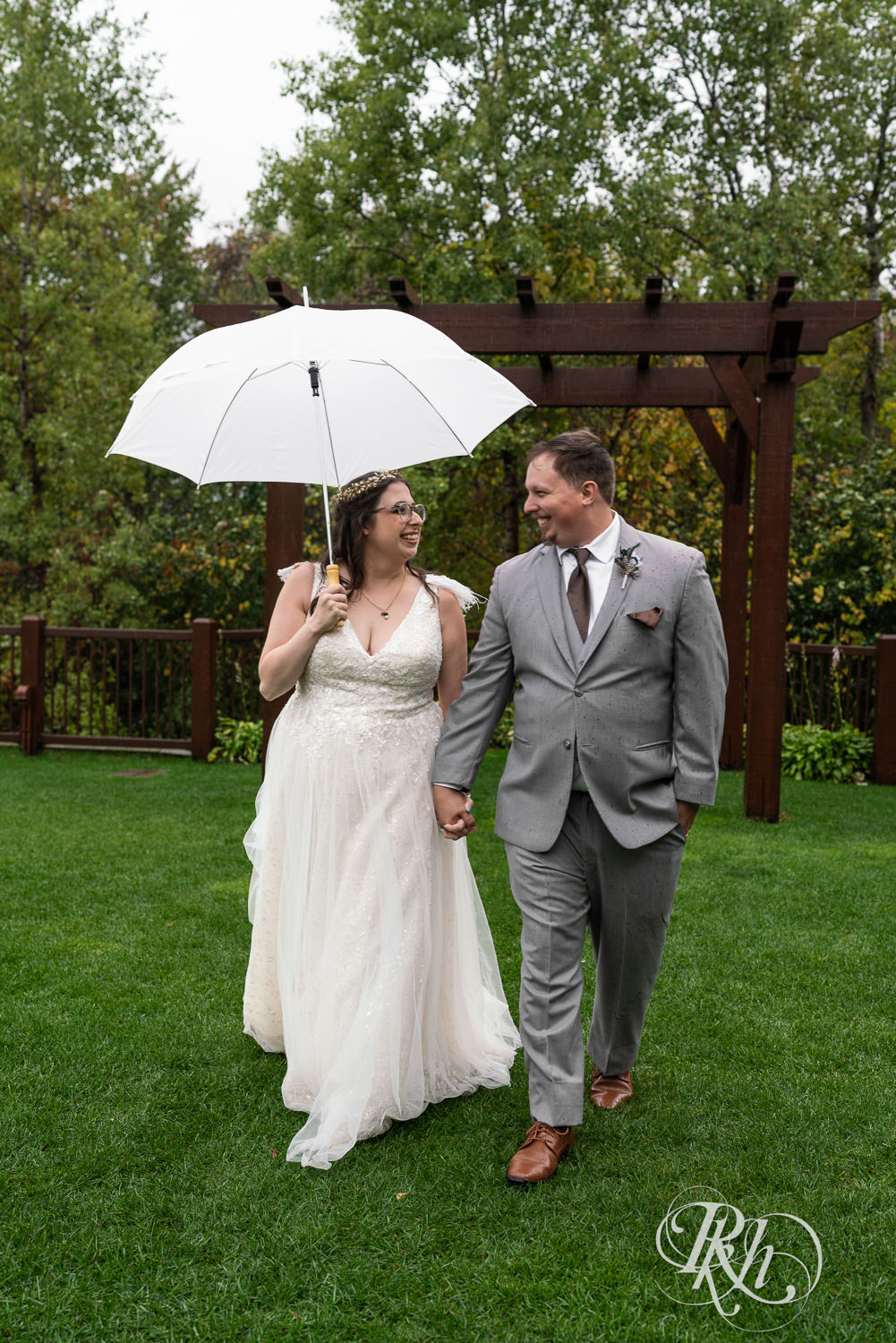 Bride and groom smile under the umbrella during rainy wedding day at Bunker Hills Event Center in Coon Rapids, Minnesota.