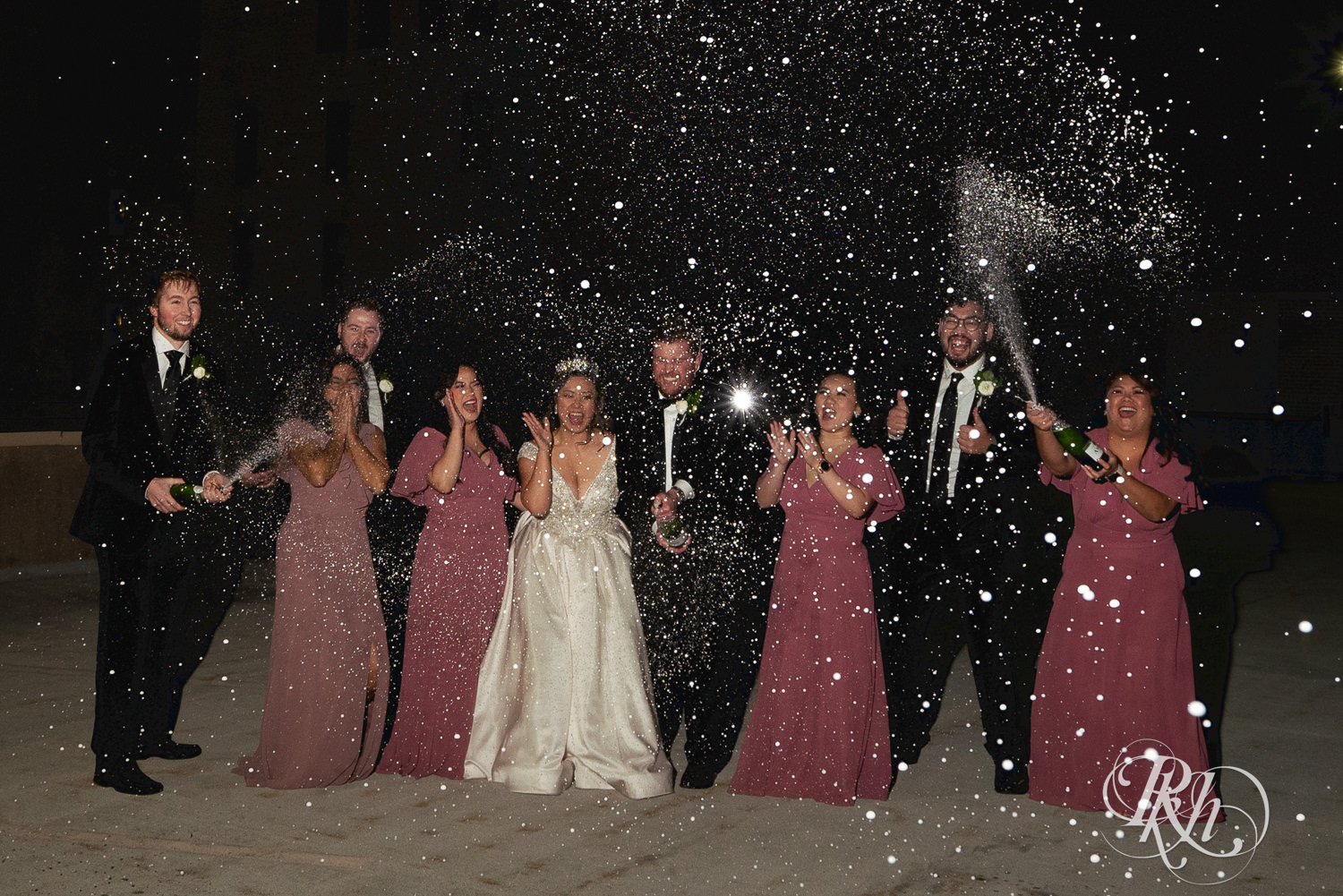 Hmong bride and groom spray champagne with their wedding party on a rooftop in Saint Paul, Minnesota.
