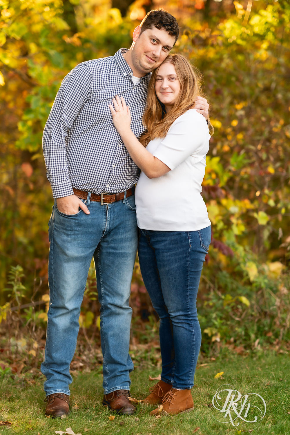 Man and woman in jeans smile during fall engagement photos at Lebanon Hills Regional Park in Eagan, Minnesota.