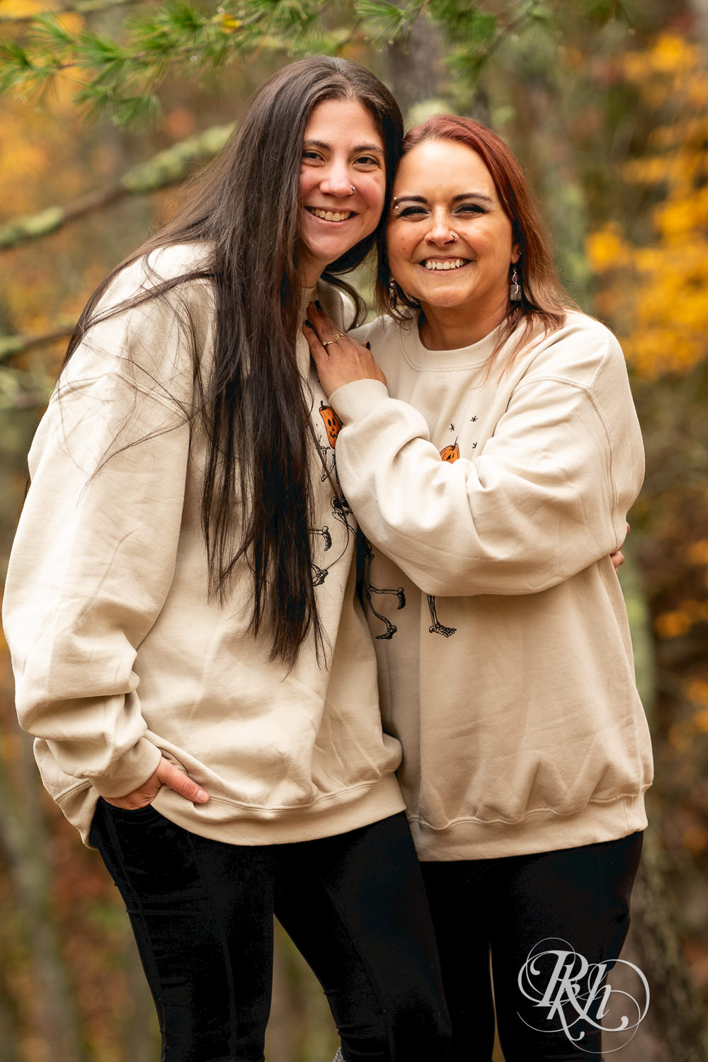 Lesbian couple in Halloween sweaters smile during fall engagement photos at Amnicon Falls in Wisconsin. 