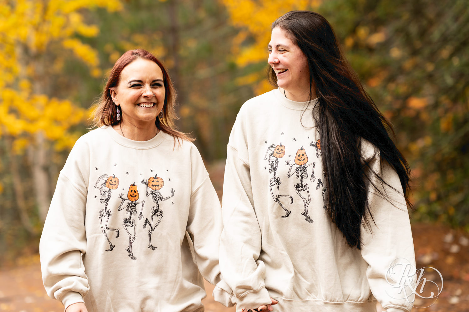 Lesbian couple in Halloween sweaters laugh during fall engagement photos at Amnicon Falls in Wisconsin. 
