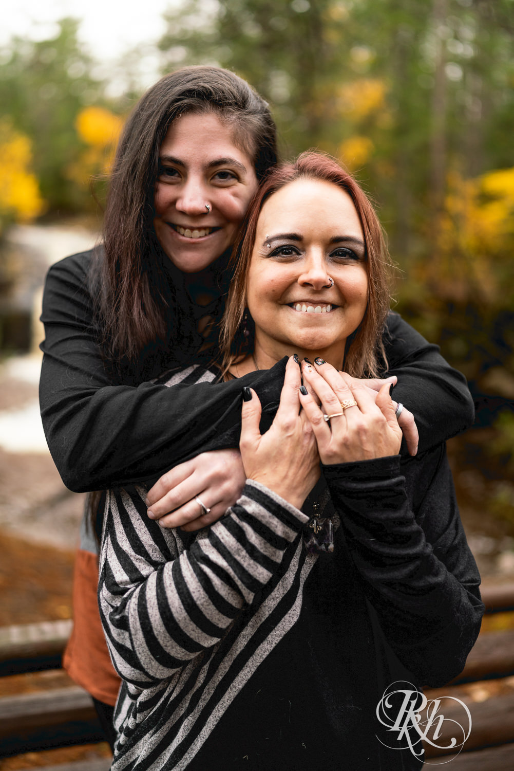Lesbian couple smiles during fall engagement photos at Amnicon Falls in Wisconsin. 