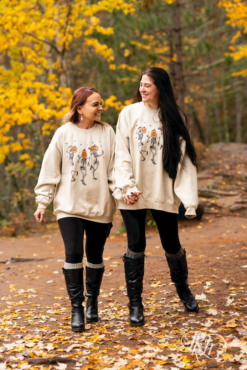 Lesbian couple in Halloween sweaters laugh during fall engagement photos at Amnicon Falls in Wisconsin. 