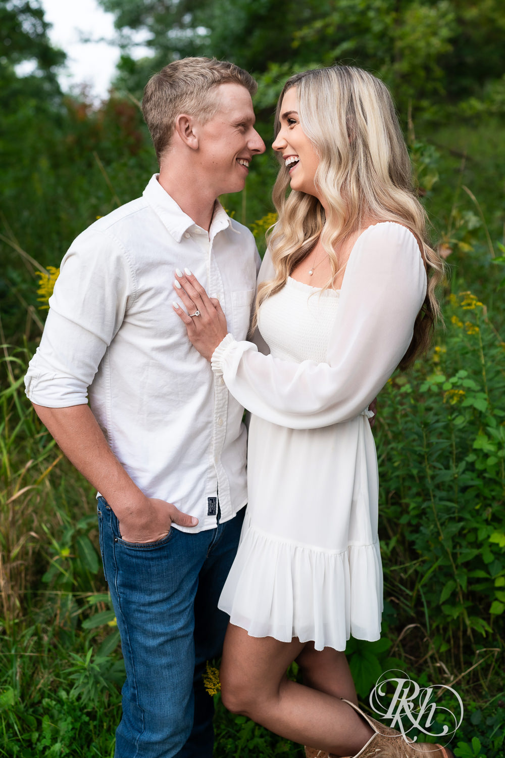 Man and woman in white and cowboy boots smile during engagement photography at Lebanon Hills Regional Park in Eagan, Minnesota.