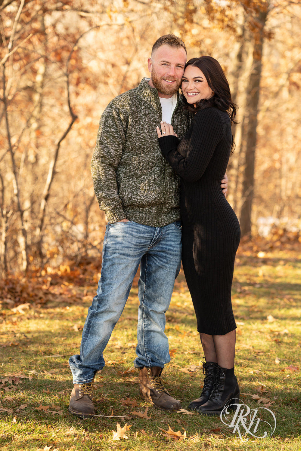 Man in sweater and jeans and woman in black dress smile at Lebanon Hills Regional Park in Eagan, Minnesota for December morning engagement photography.