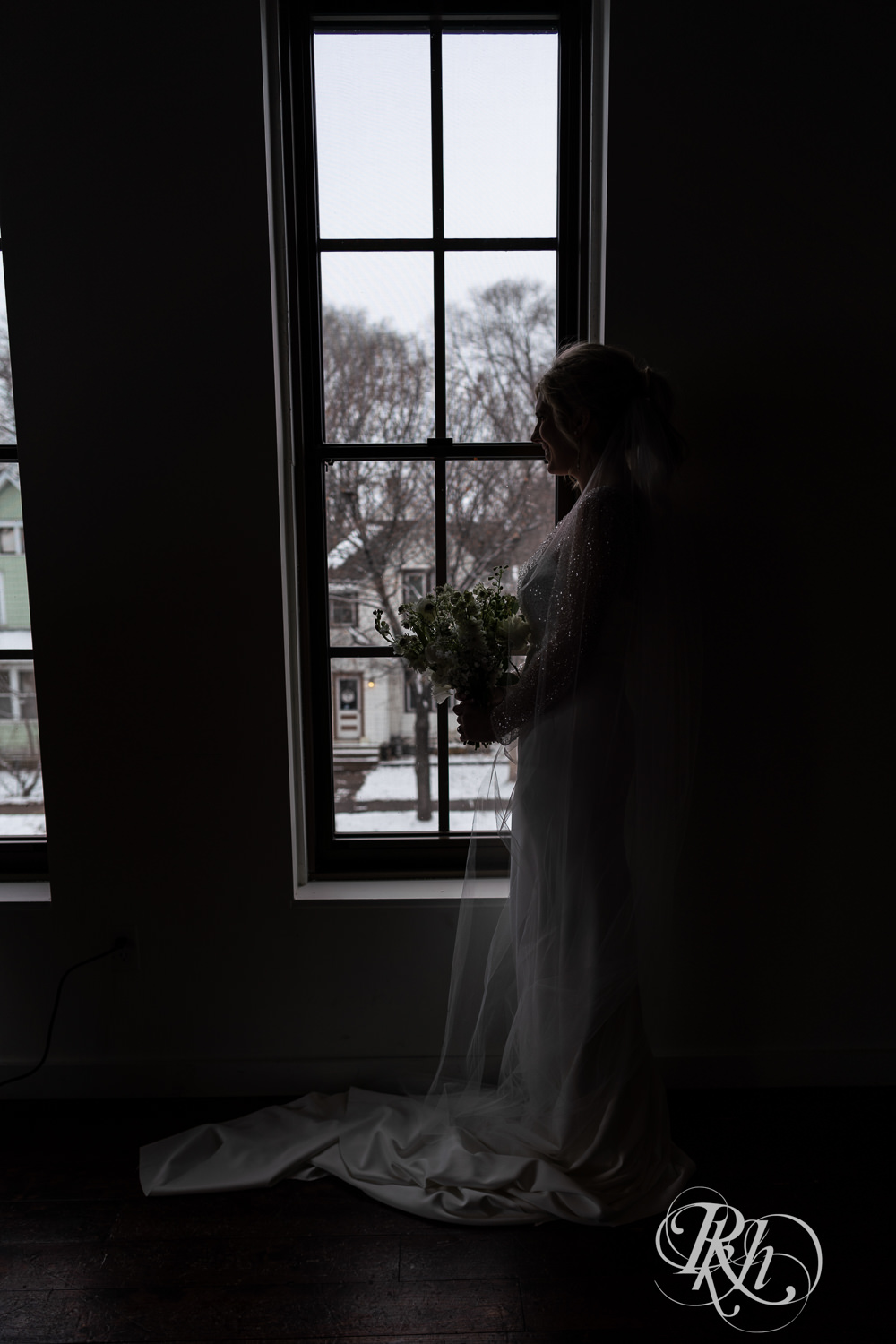Bride smiles holding flowers by windows at Gatherings at Station 10 in Saint Paul, Minnesota on winter wedding day.