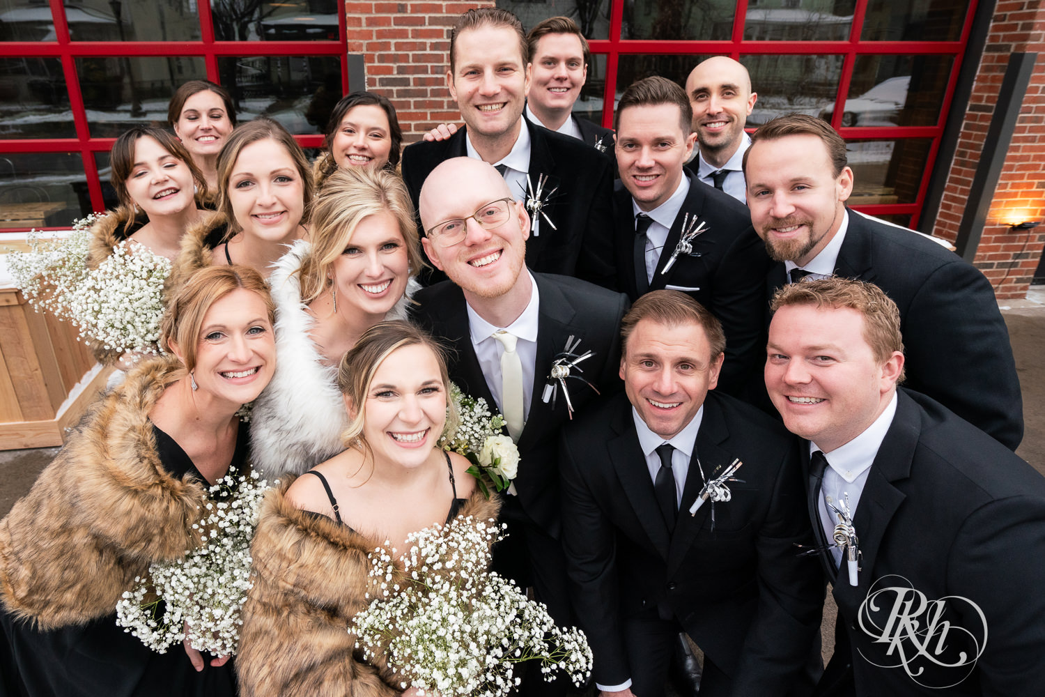 Wedding party smiles with bride and groom in front of Gatherings at Station 10 in Saint Paul, Minnesota on winter wedding day.