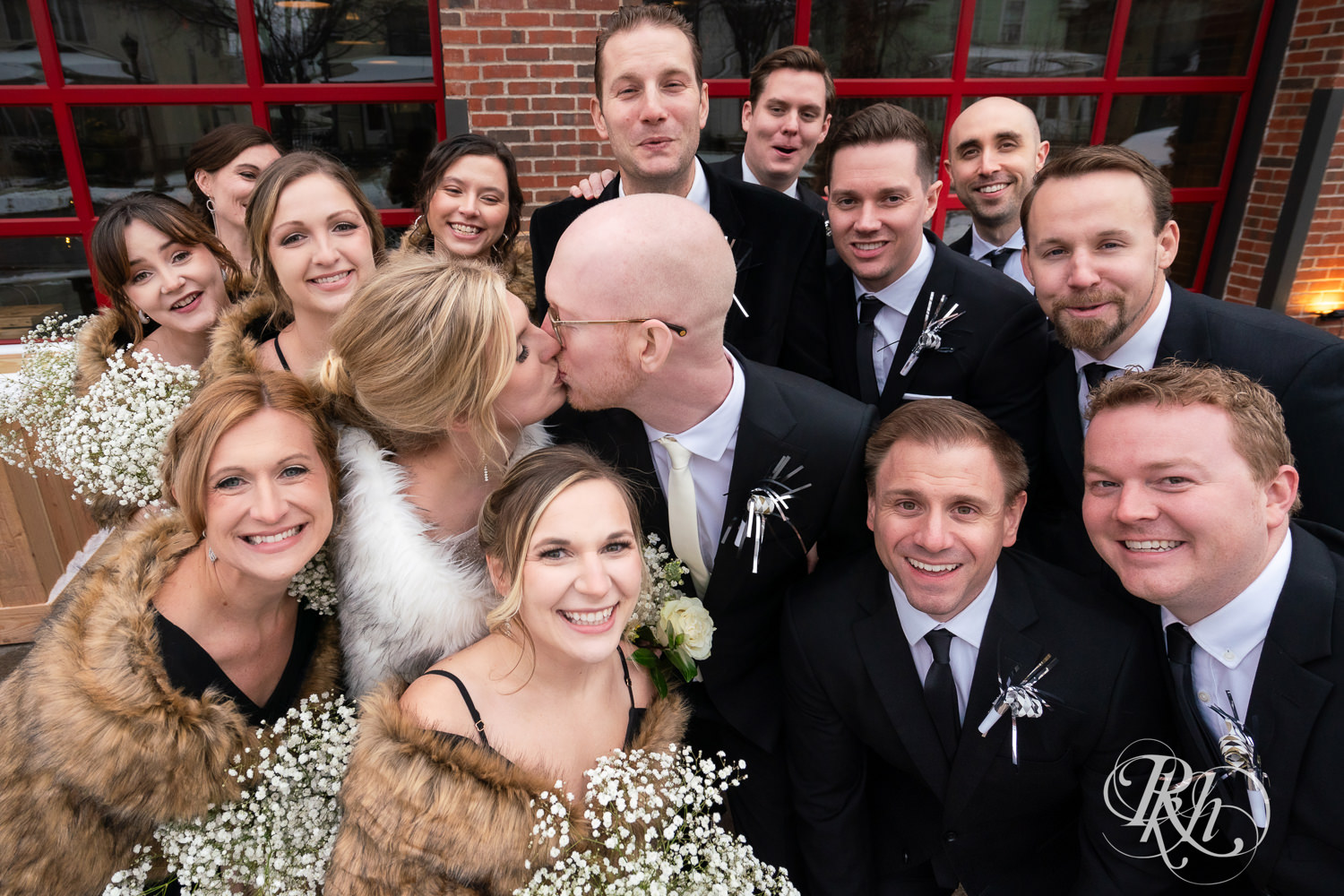 Wedding party smiles with bride and groom in front of Gatherings at Station 10 in Saint Paul, Minnesota on winter wedding day.