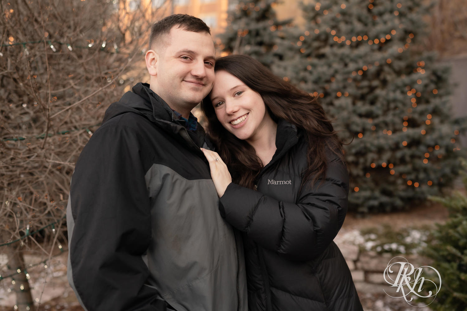 Man and woman in jackets smile during winter engagement photos at the Saint Paul Hotel in Saint Paul, Minnesota.
