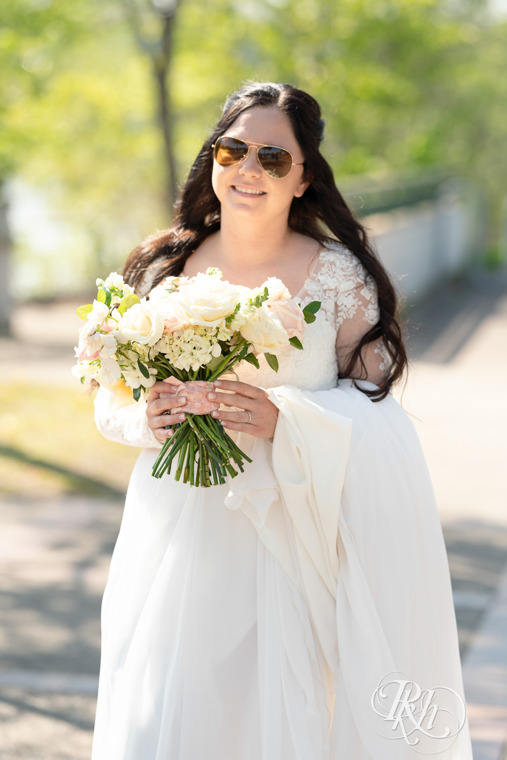 Bride walks towards groom while wearing sunglasses in Boom Island Park in Minneapolis, Minnesota.