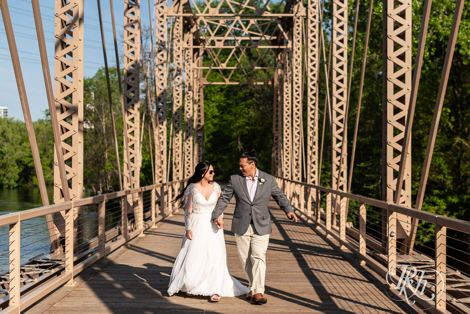 Bride and groom walk across bridge on wedding day in Boom Island Park in Minneapolis, Minnesota.