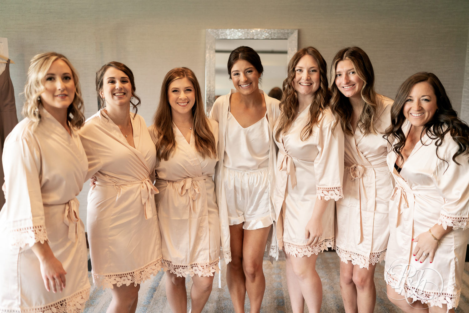 Bride smiling with her bridesmaids in neutral colored robes while getting ready on her wedding day.