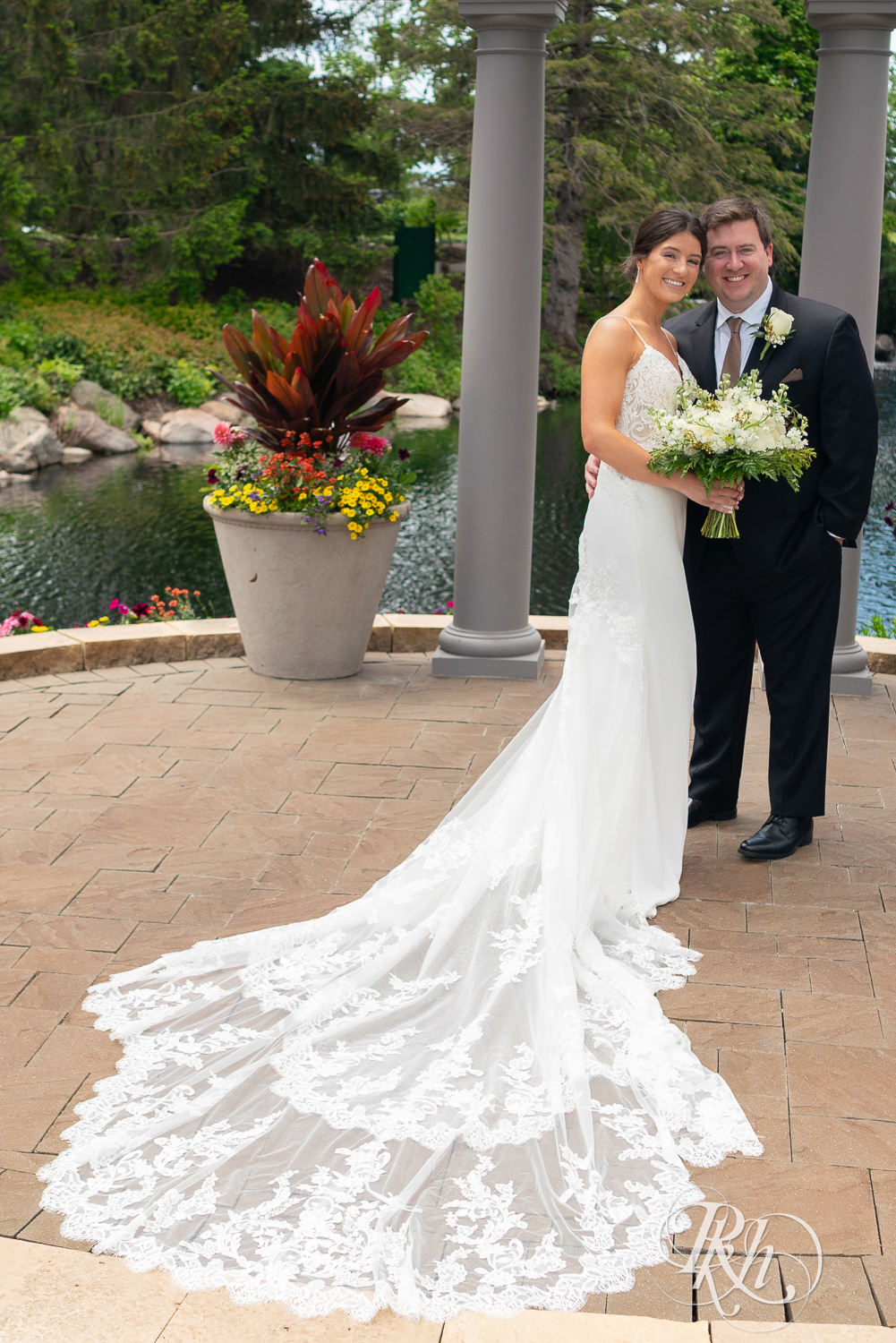 Bride and groom smile in front of water on wedding day at Olympic Hills Golf Club in Eden Prairie, Minnesota.