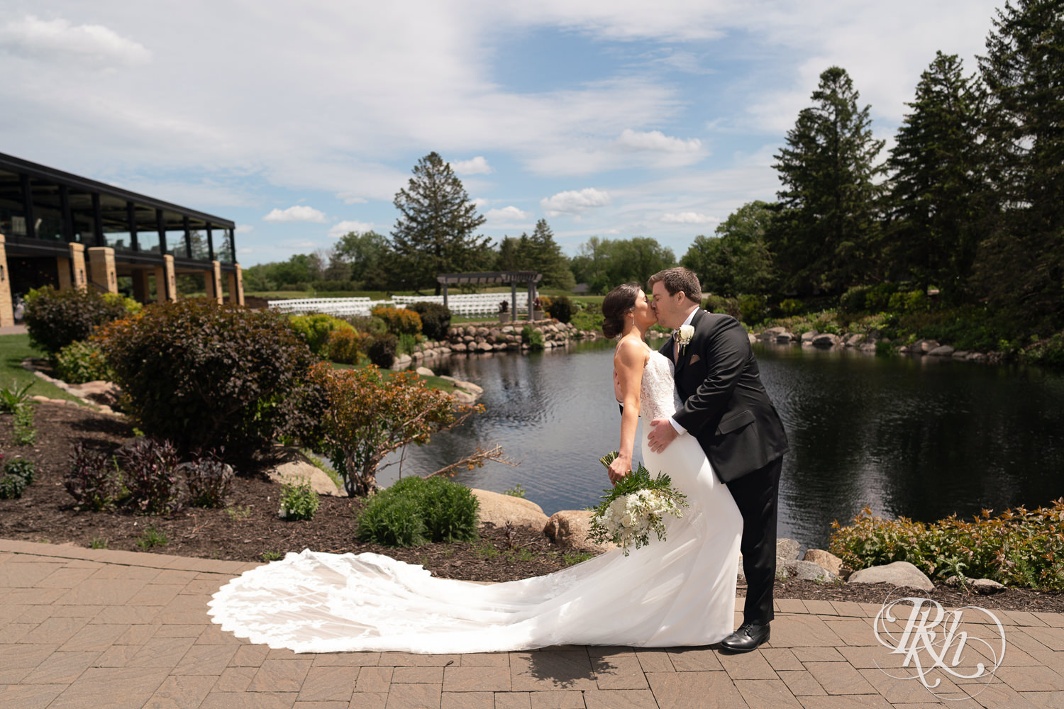 Bride and groom kiss in front of water on wedding day at Olympic Hills Golf Club in Eden Prairie, Minnesota.