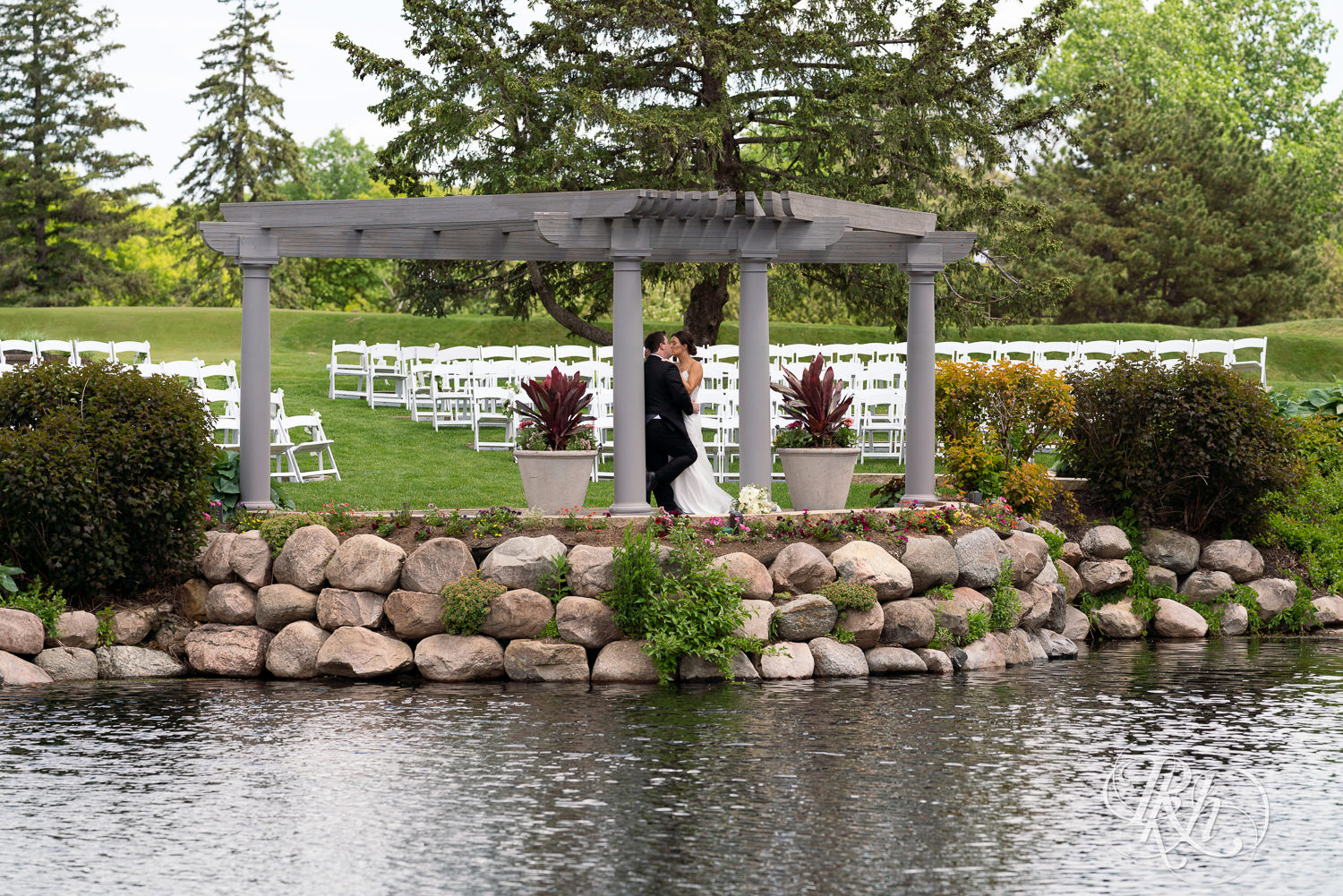 Bride and groom kiss next to the water at Olympic Hills Golf Club in Eden Prairie, Minnesota.