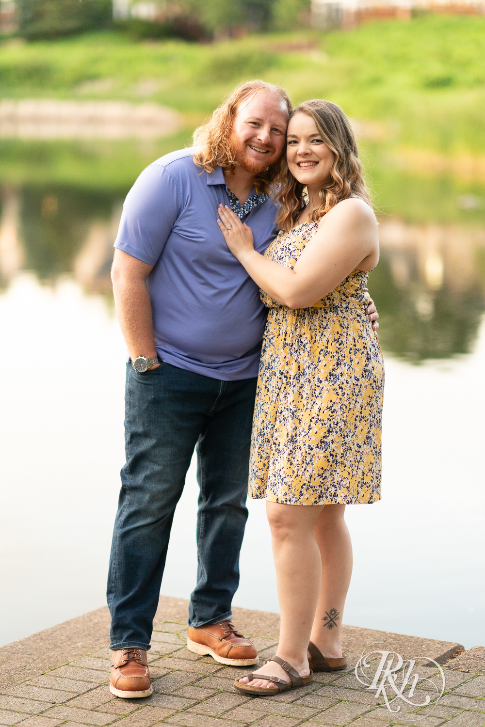 Man in blue shirt and woman in flower dress smile in front of the water at Centennial Lakes Park in Edina, Minnesota.