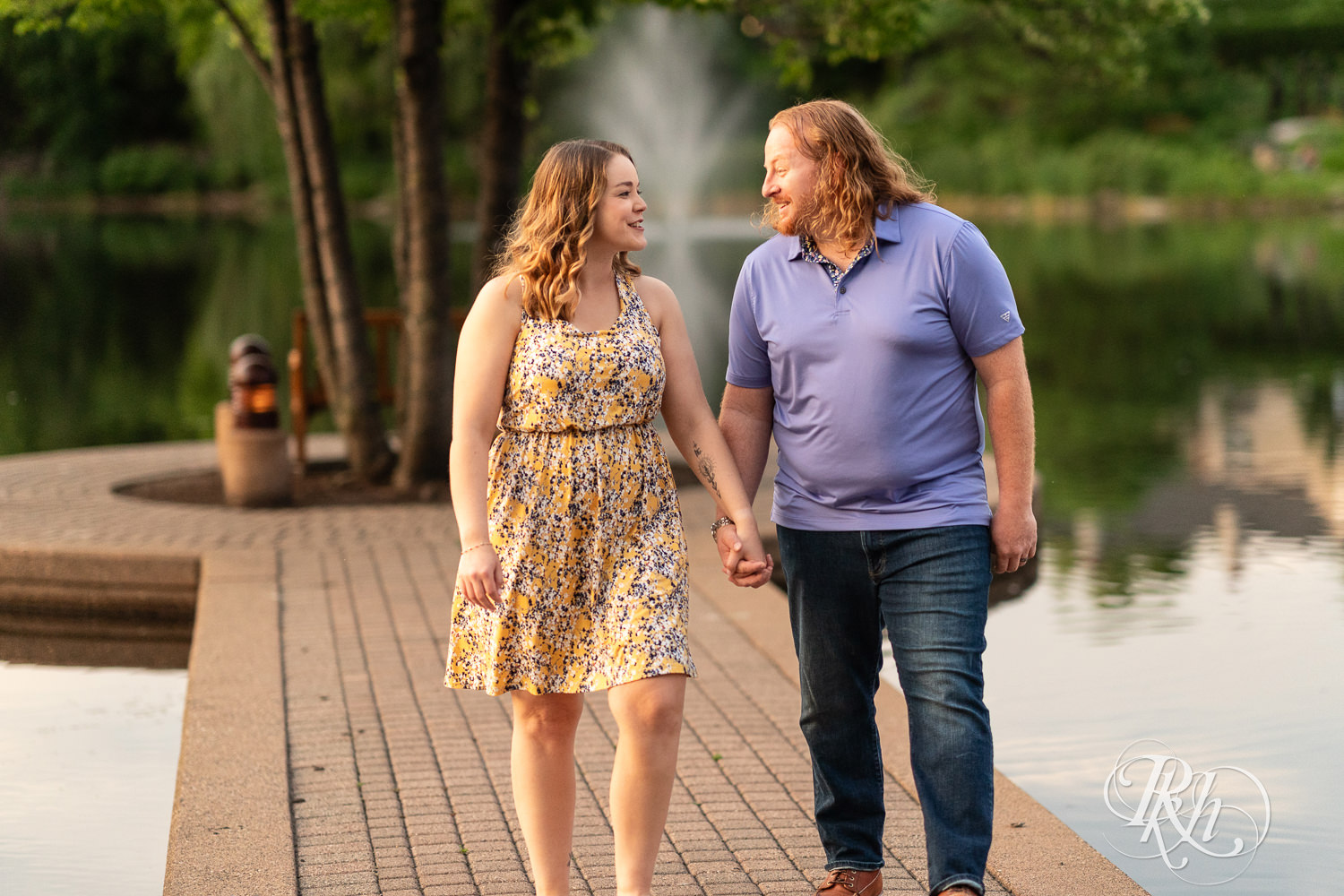 Man in blue shirt and woman in flower dress smile in front of the water at Centennial Lakes Park in Edina, Minnesota.