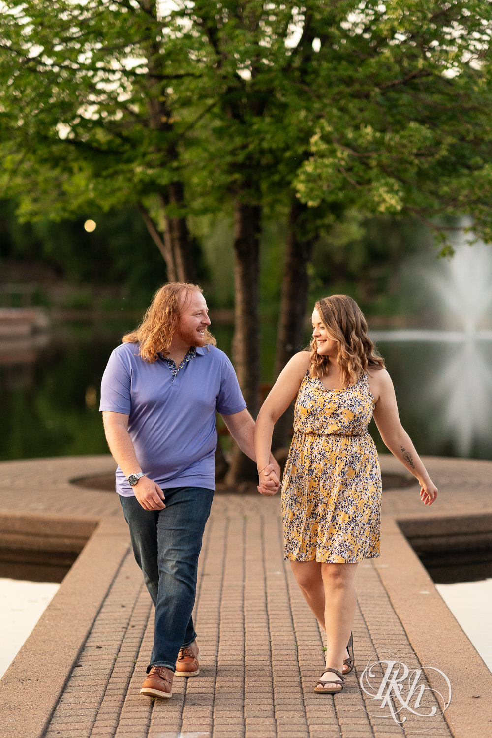 Man in blue shirt and woman in flower dress smile in front of the water at Centennial Lakes Park in Edina, Minnesota.