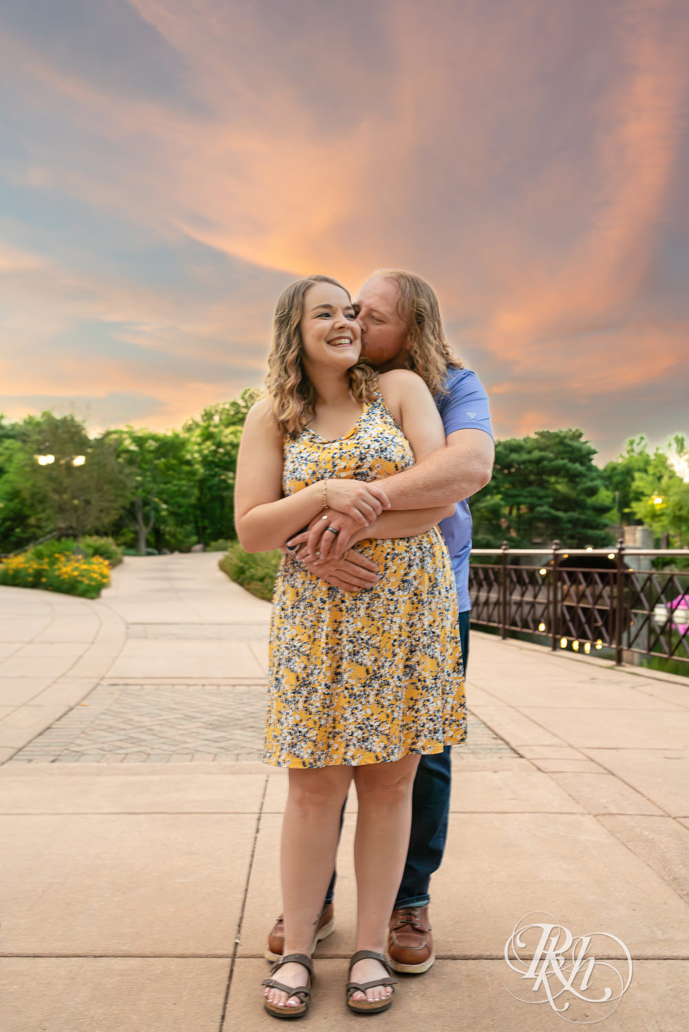 Man in blue shirt and woman in flower dress kiss at sunset at Centennial Lakes Park in Edina, Minnesota.