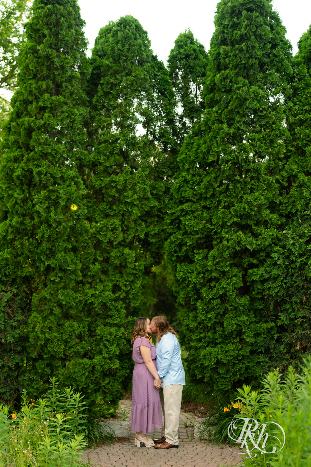 Man in blue shirt and woman in purple dress kiss at sunset at Centennial Lakes Park in Edina, Minnesota.