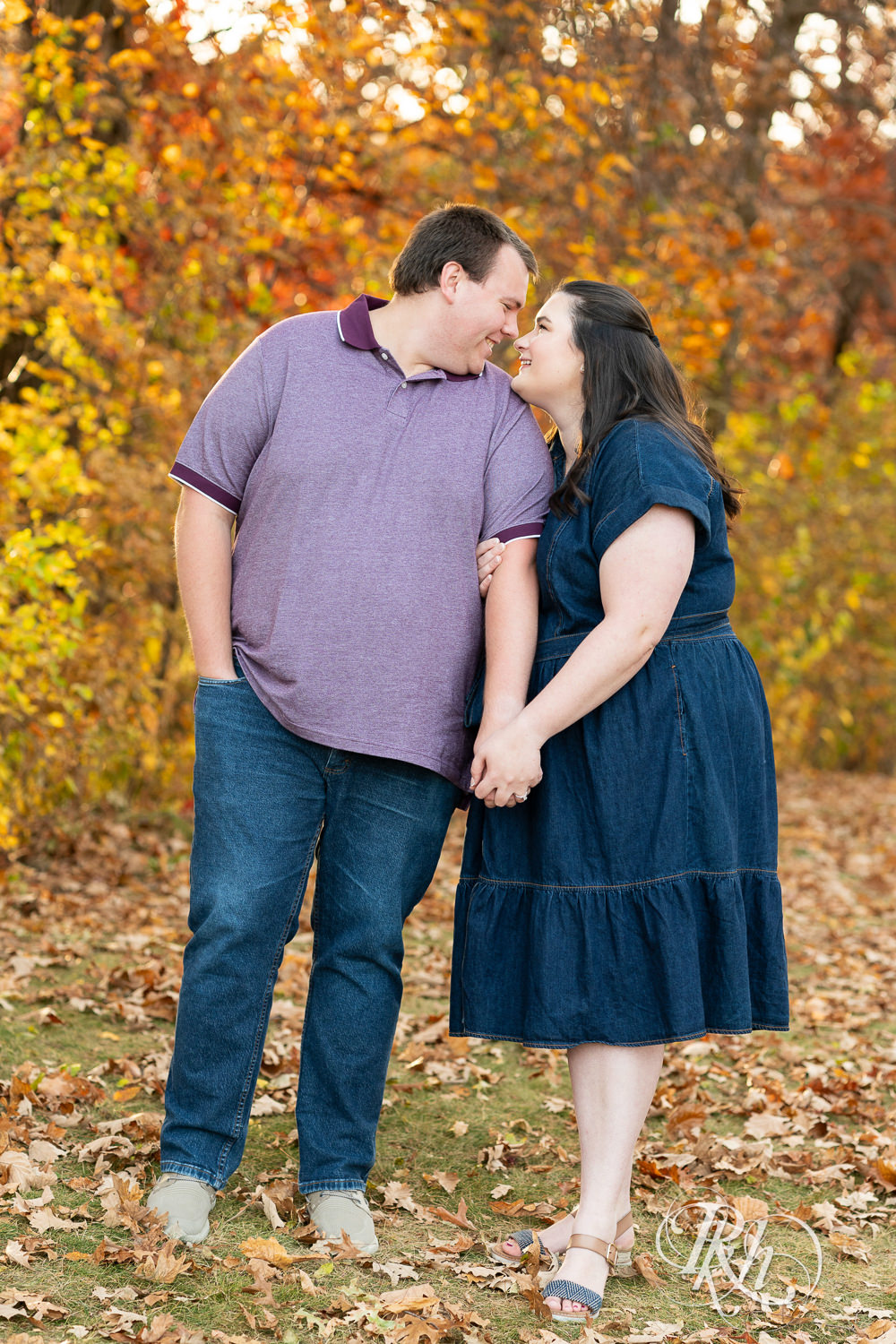 Plus size man and woman in blue dress smile at each other during engagement photos at Lebanon Hills Regional Park in Eagan, Minnesota.