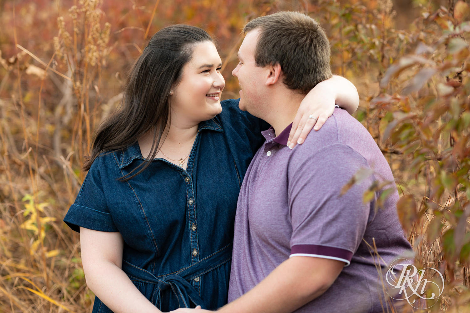 Plus size man and woman in blue dress smile at each other during engagement photos at Lebanon Hills Regional Park in Eagan, Minnesota.