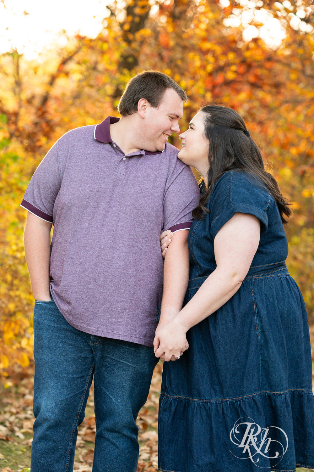 Plus size man and woman in blue dress smile at each other during engagement photos at Lebanon Hills Regional Park in Eagan, Minnesota.