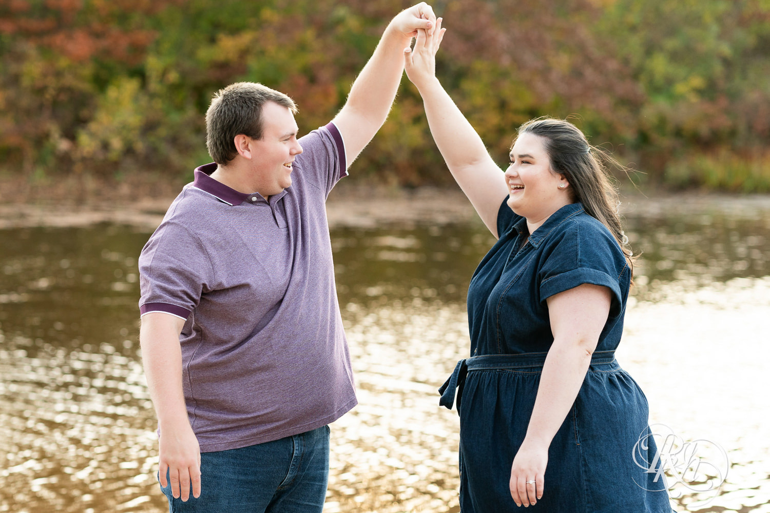 Plus size man and woman dance on beach during engagement photos at Lebanon Hills Regional Park in Eagan, Minnesota.