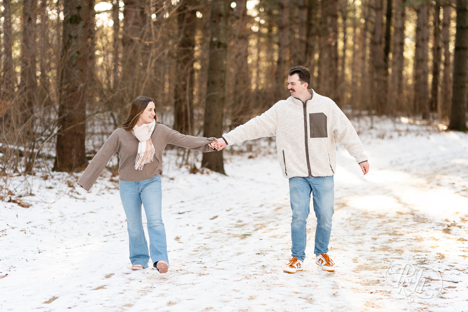 Man and woman walk in snow during winter engagement photos at Lebanon Hills Regional Park in Eagan, Minnesota.