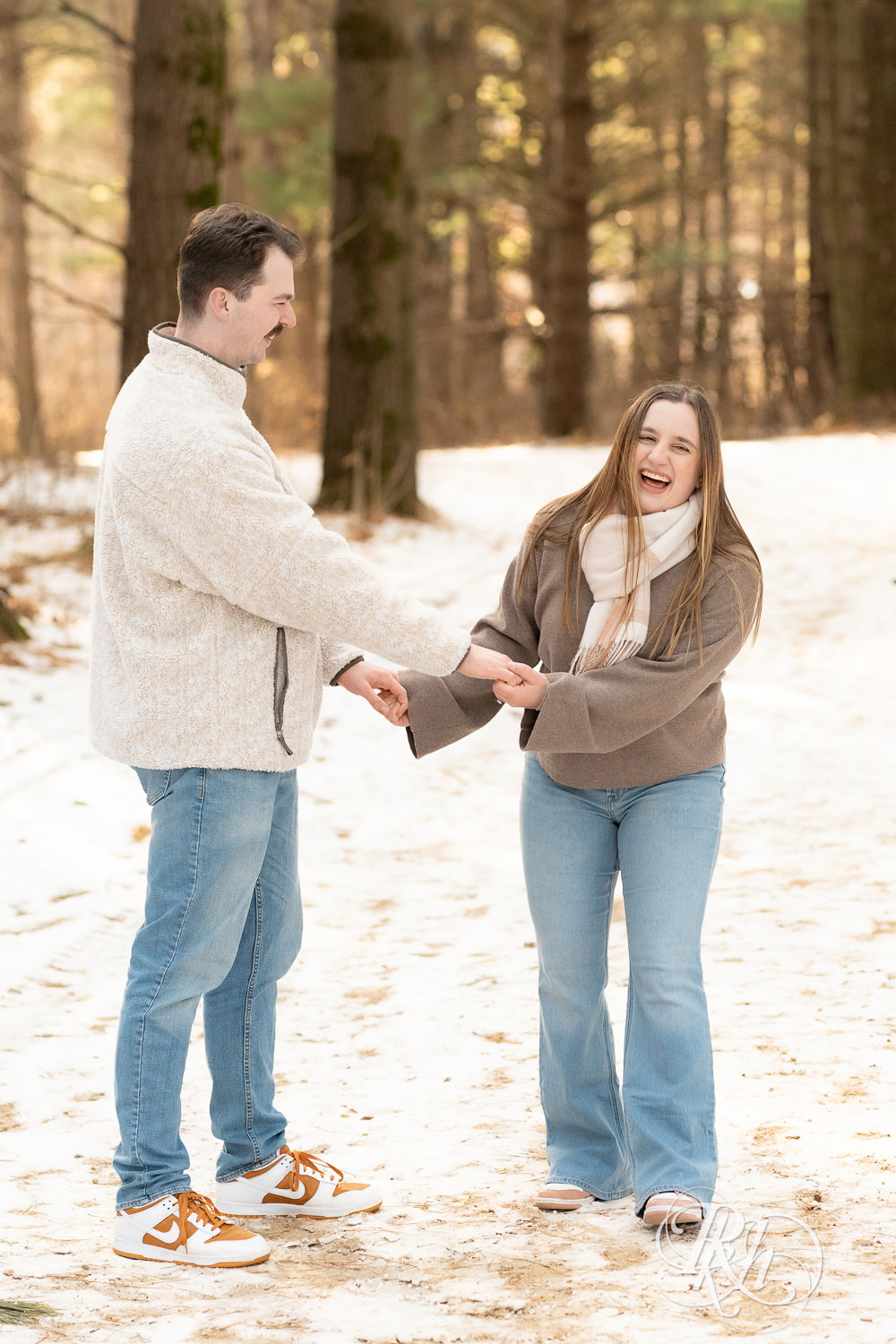 Man and woman laugh in forest during winter engagement photos at Lebanon Hills Regional Park in Eagan, Minnesota.