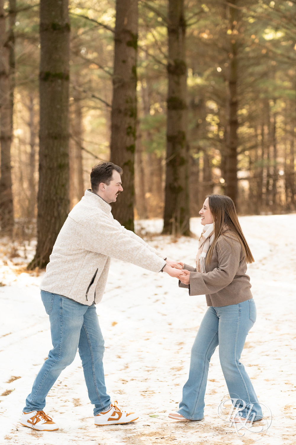 Man and woman laugh in forest during winter engagement photos at Lebanon Hills Regional Park in Eagan, Minnesota.