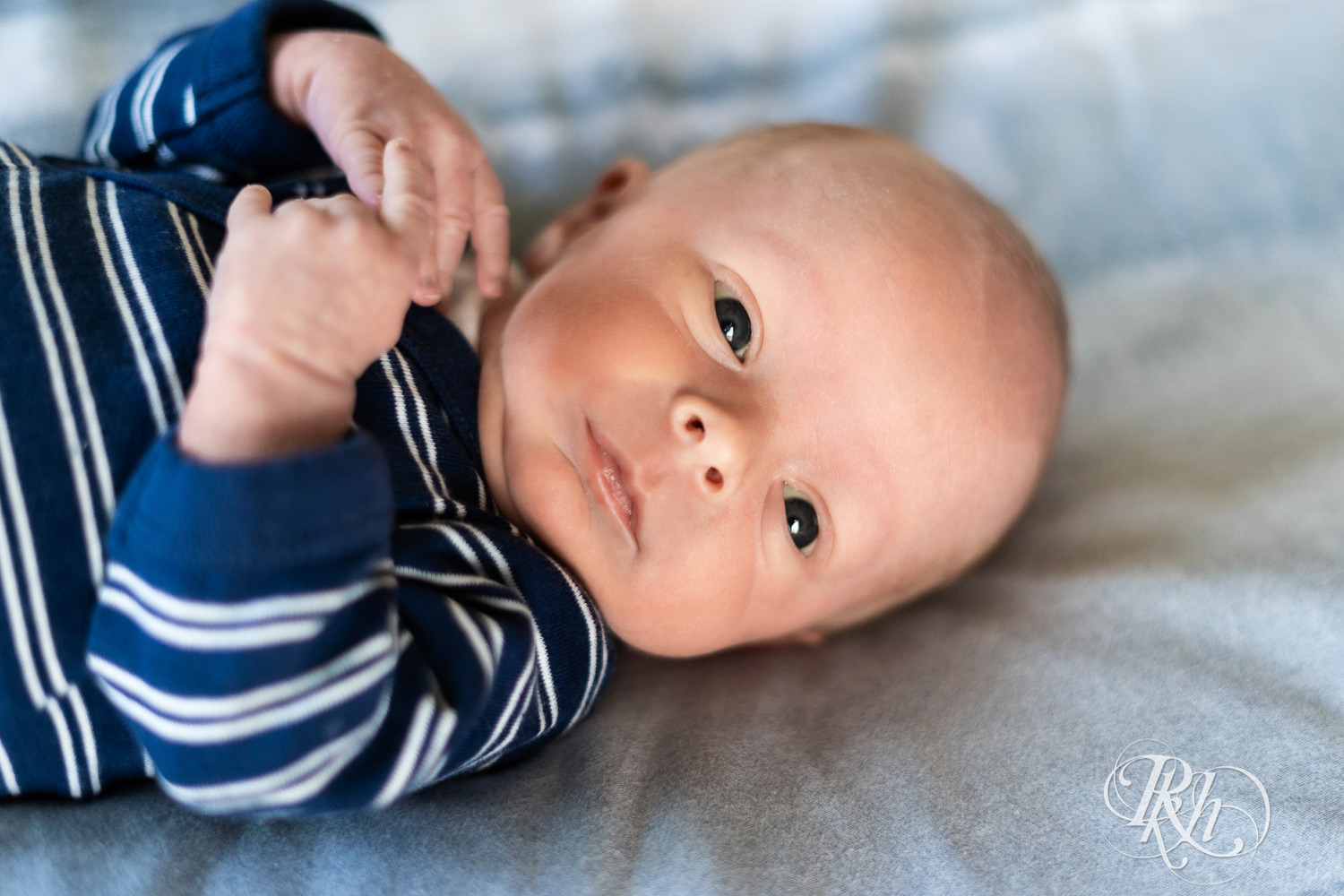 Baby dressed in blue and white stripped onesie smiles during baby photography session.