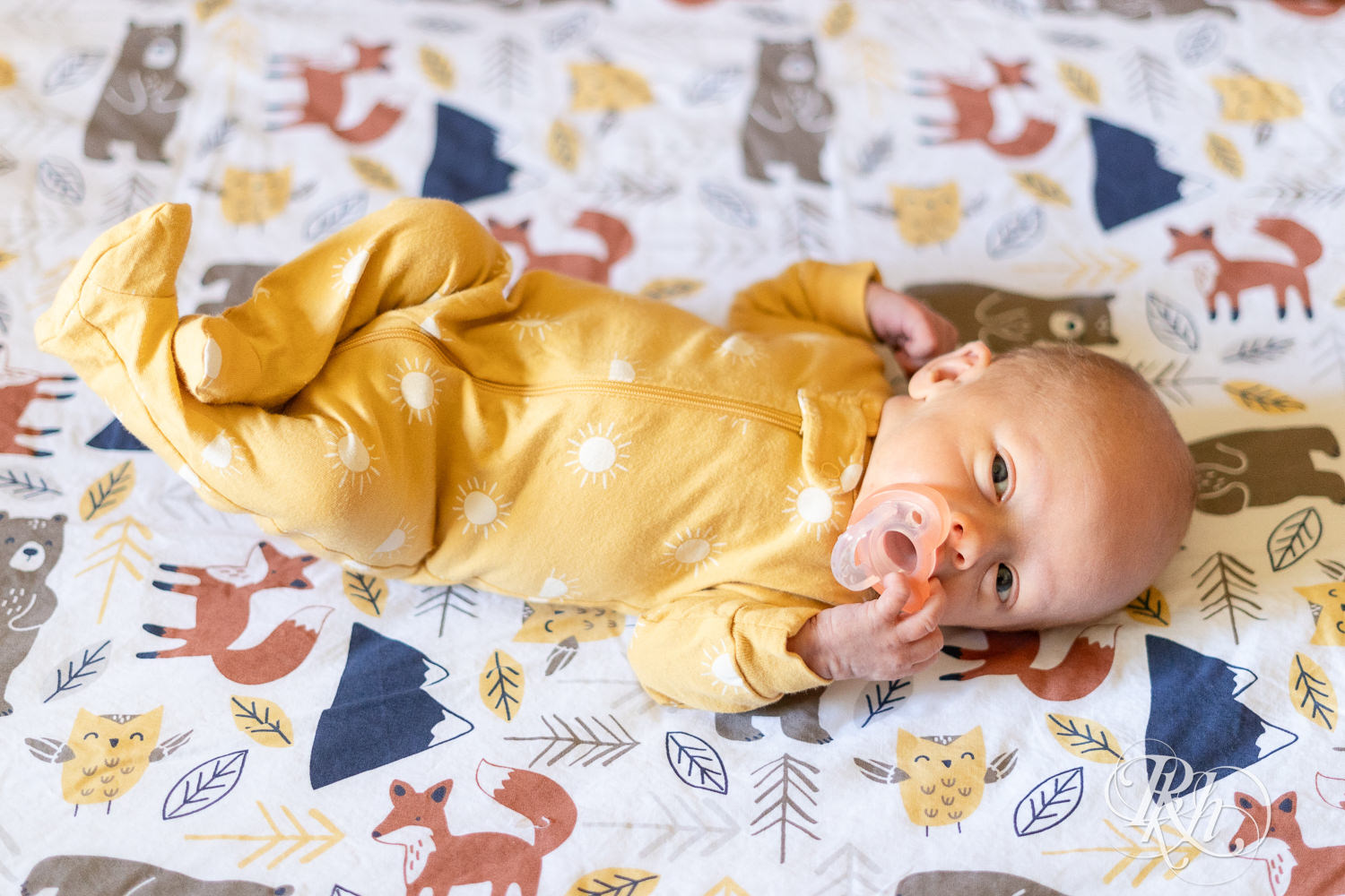 Baby dressed in yellow onesie smiles during newborn photography in Maple Grove, Minnesota.