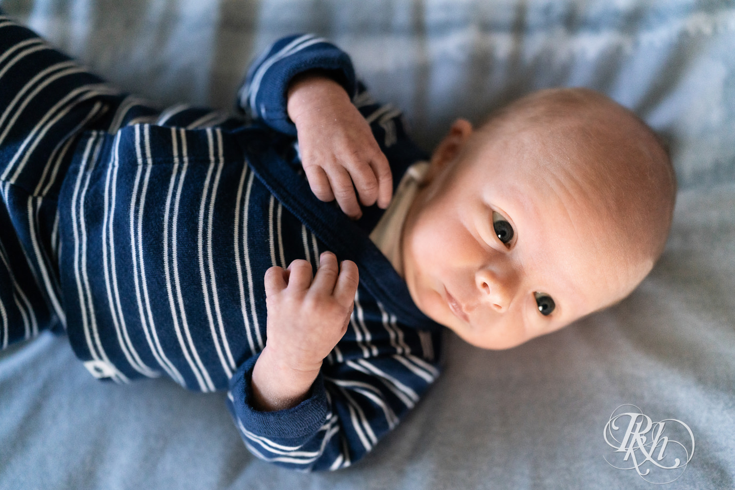 Baby dressed in blue and white stripped onesie smiles during baby photography session.