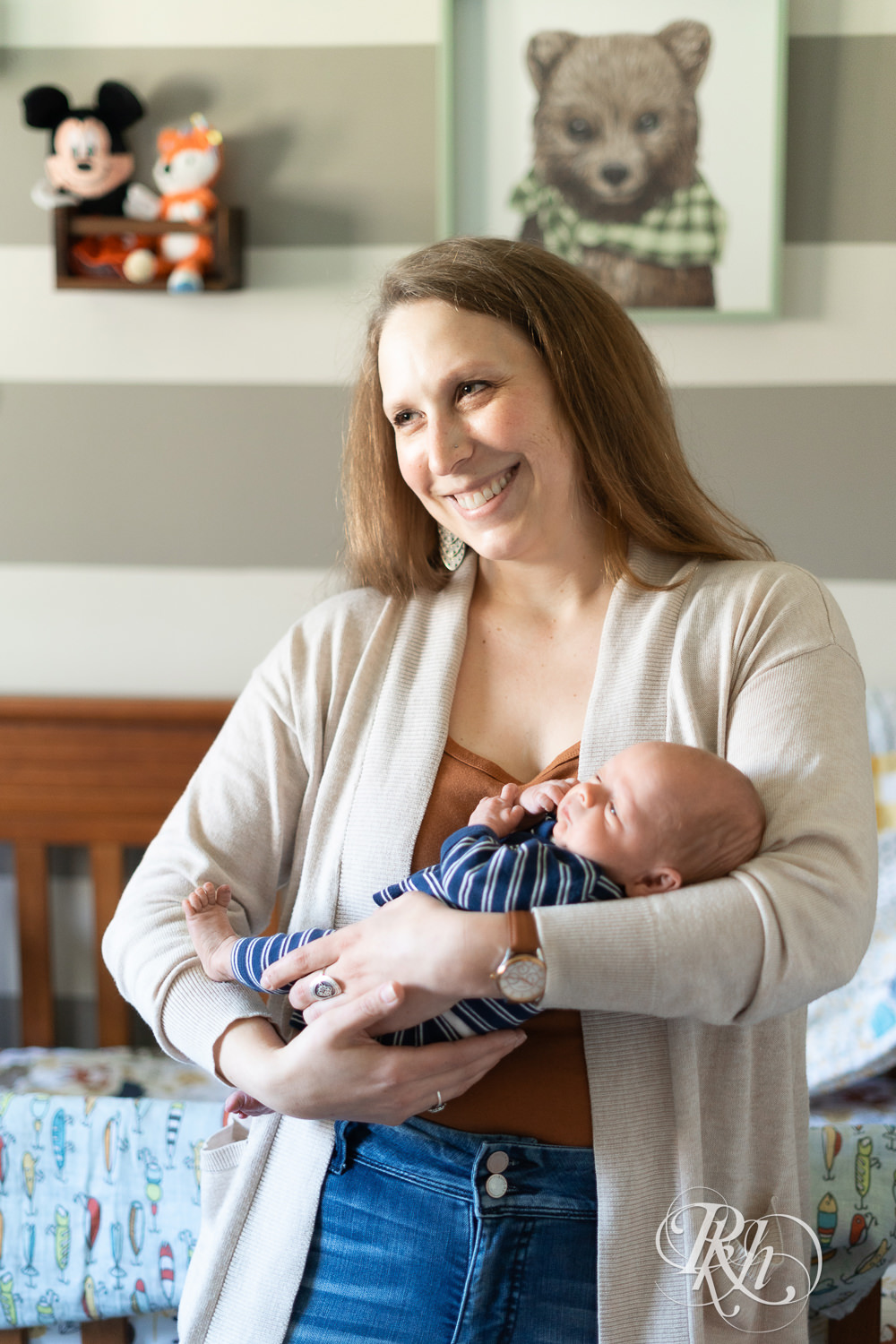 Mom smiles while holding baby in the nursery. 