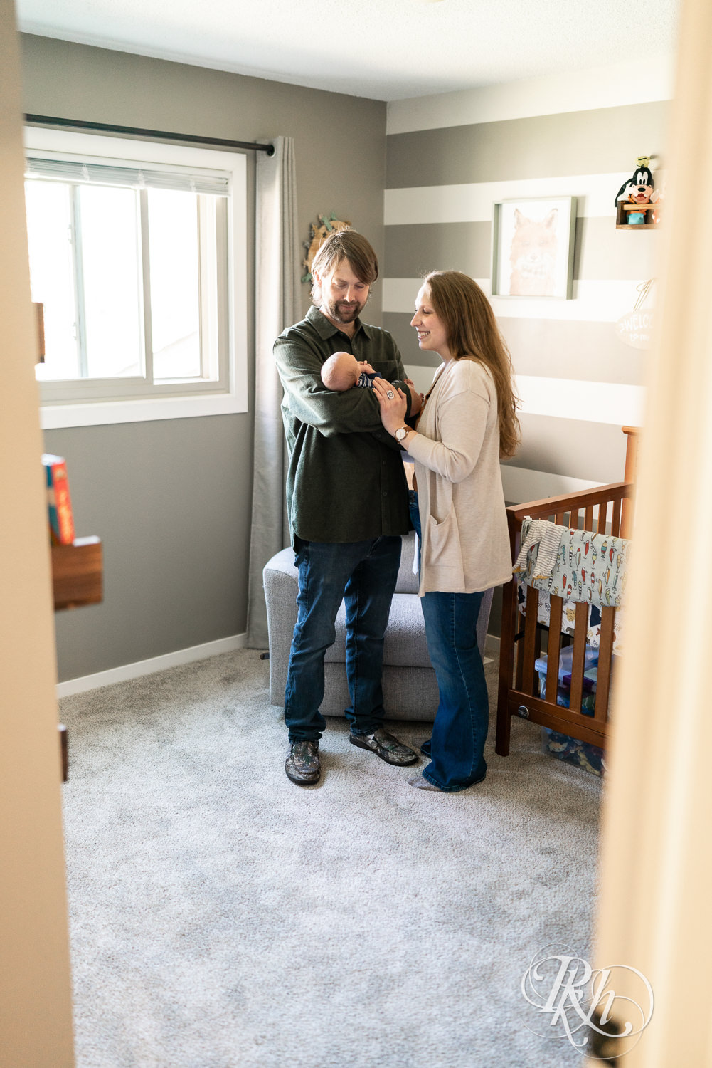 Mom and dad smile while holding baby in the nursery in Maple Grove, Minnesota.