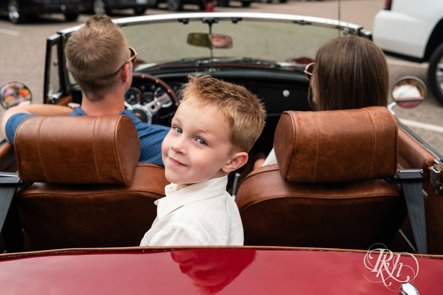 Son smiles from the backseat of a red MG with parents in the front in Eagan, Minnesota.