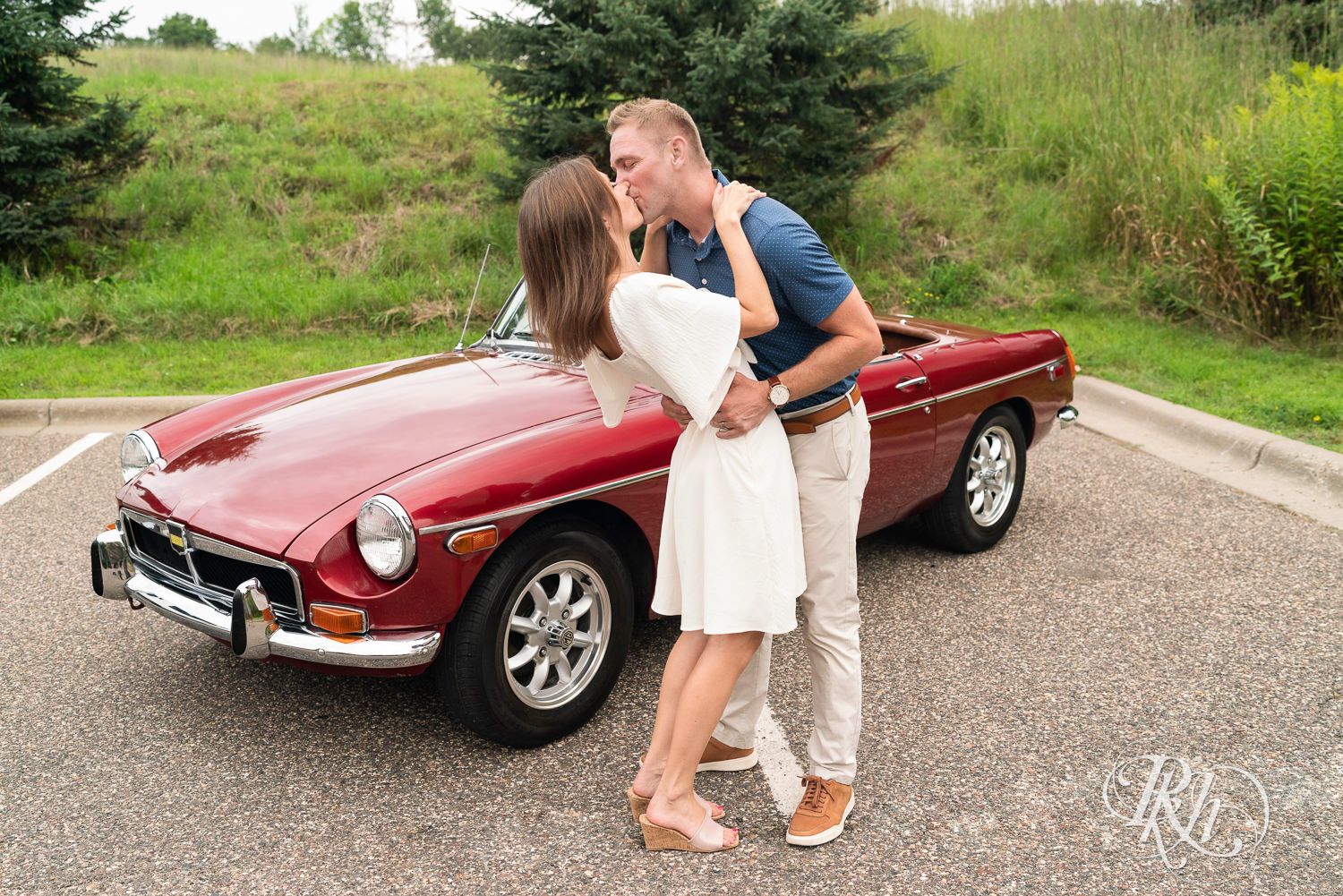 Man and woman in white dress dip and kiss in front of a classic red MG convertible in Eagan, Minnesota.