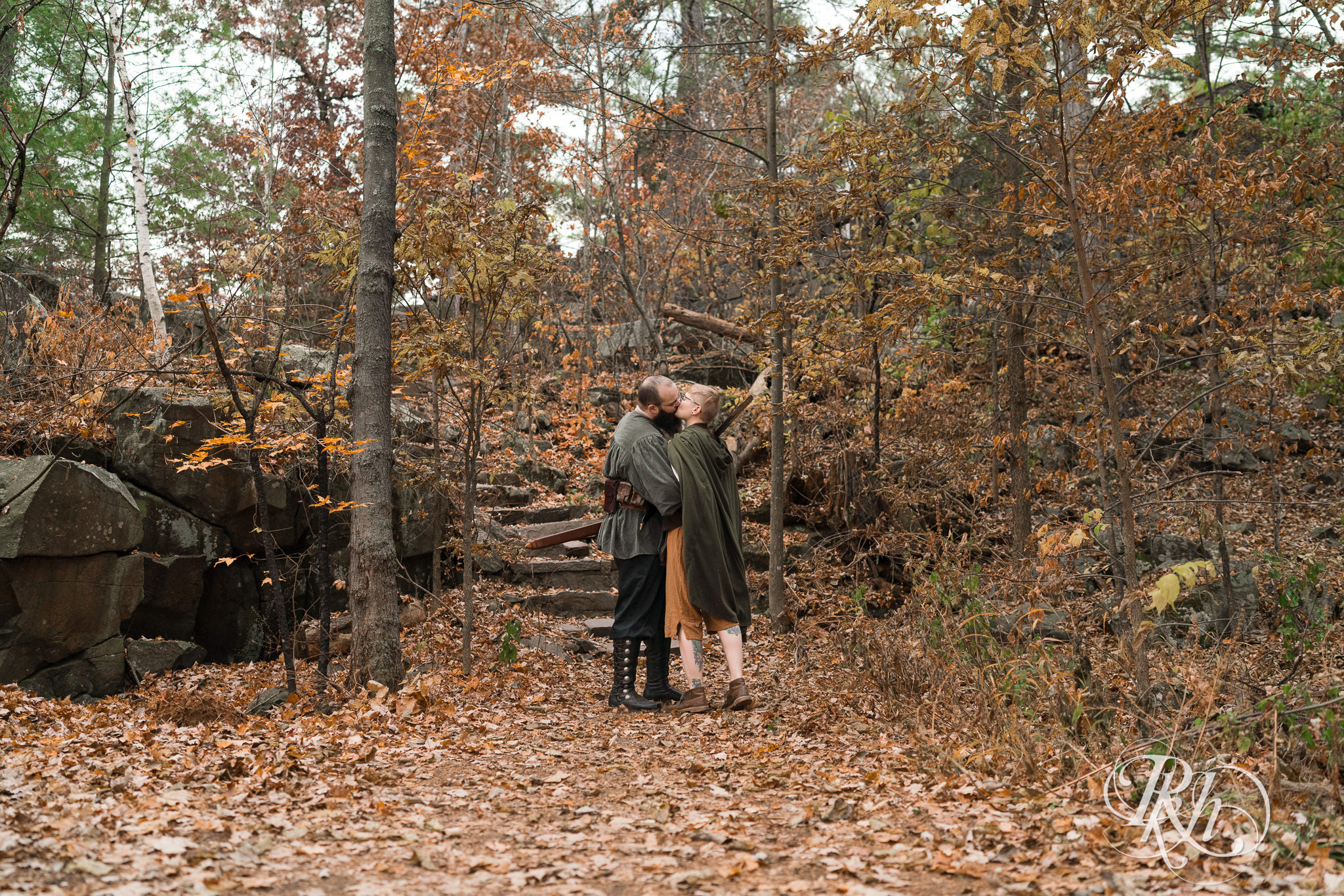 Man and non binary person in Renaissance outfits kiss amongst trees in Taylor's Falls, Minnesota.