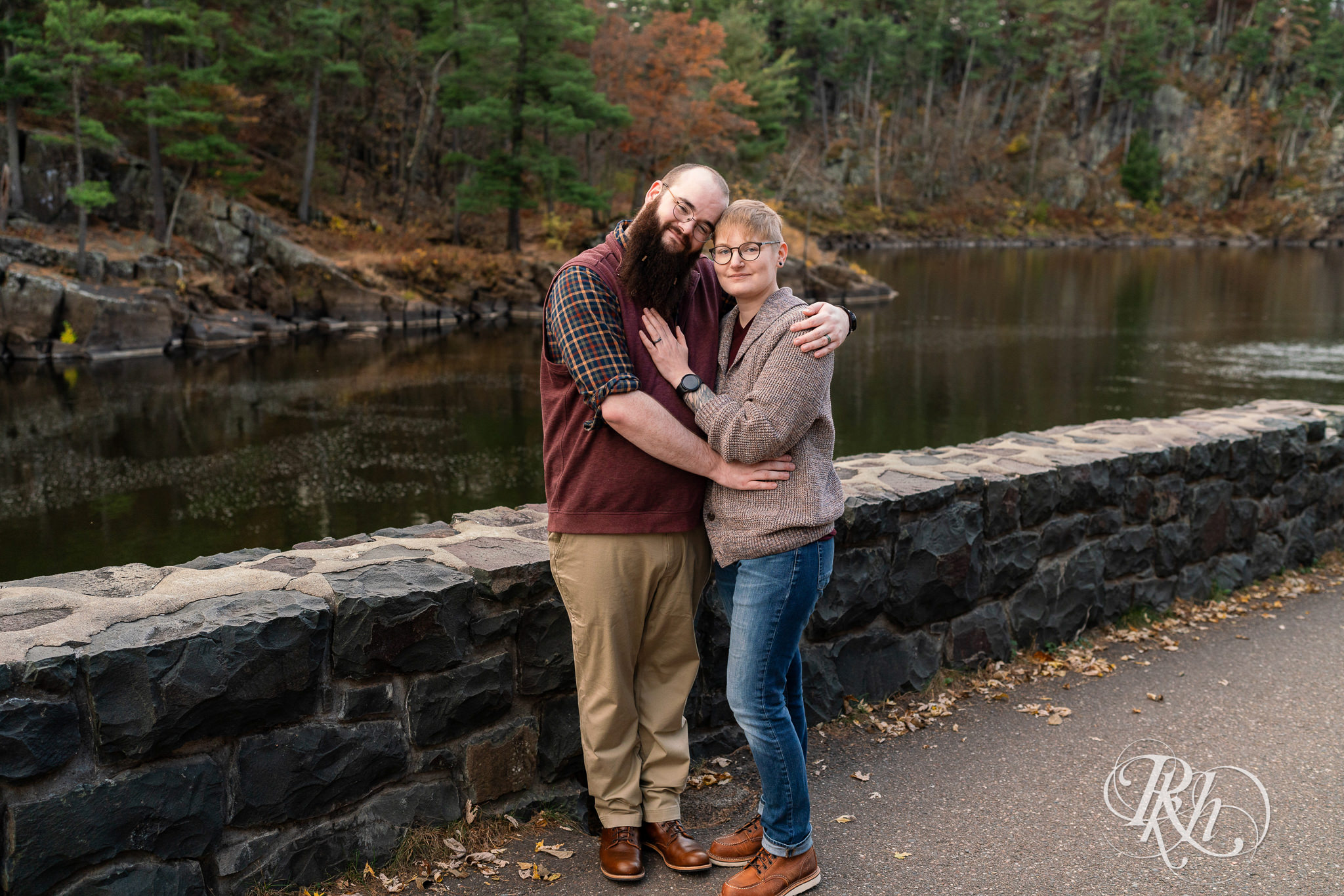 Man and non binary person smile along river during engagement photos in Taylor's Falls, Minnesota.