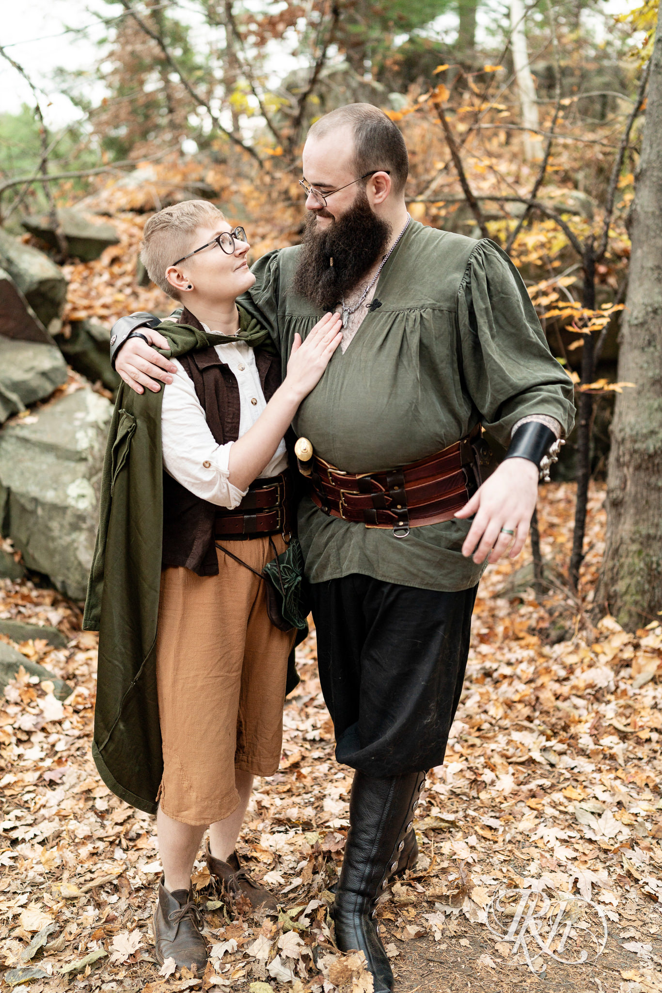 Man and non binary person in Renaissance outfits smile together on a cloudy day in Taylor's Falls, Minnesota.