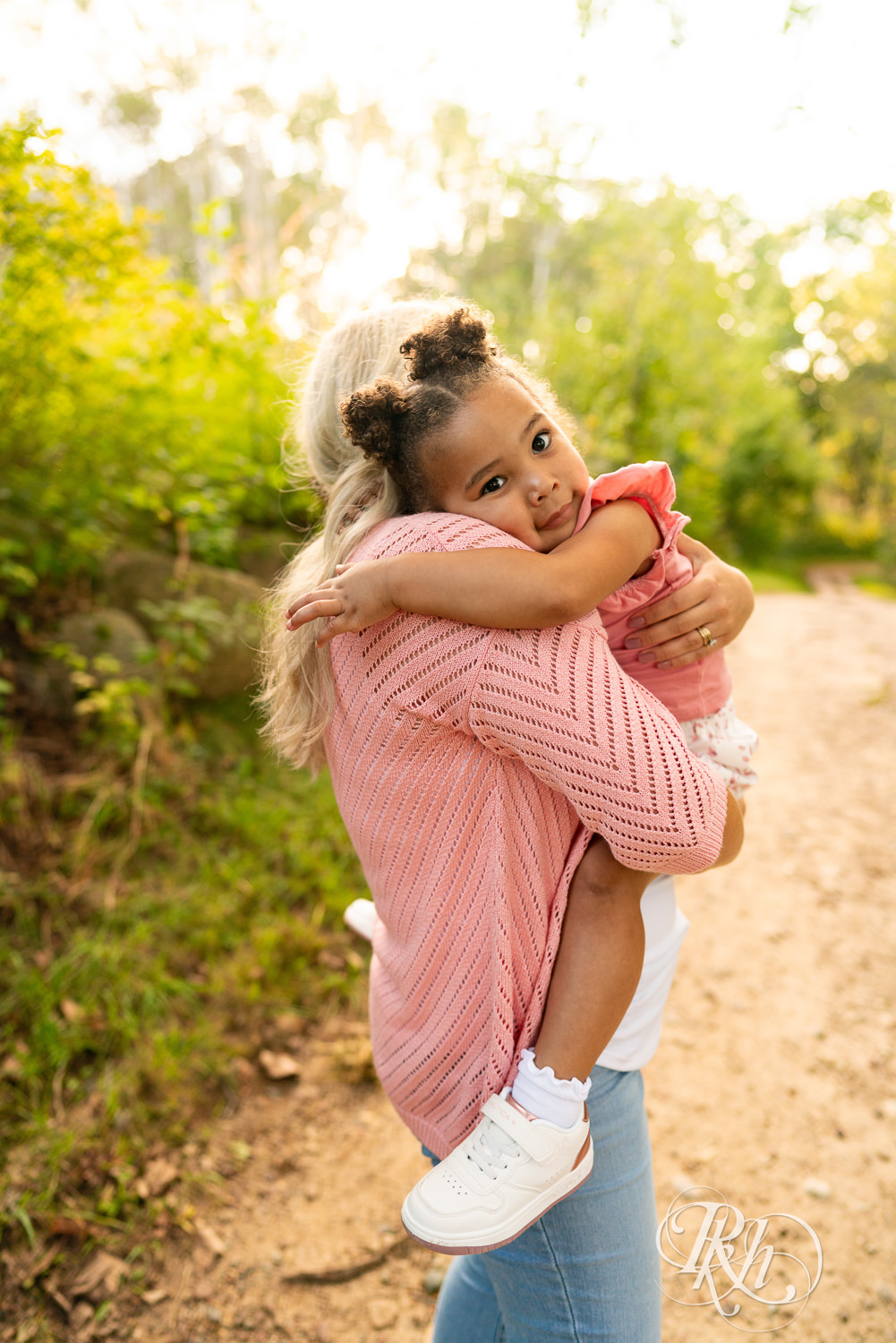 Little black girl clings to her mom as she carries her down a nature trail during sunset in Eagan, Minnesota.