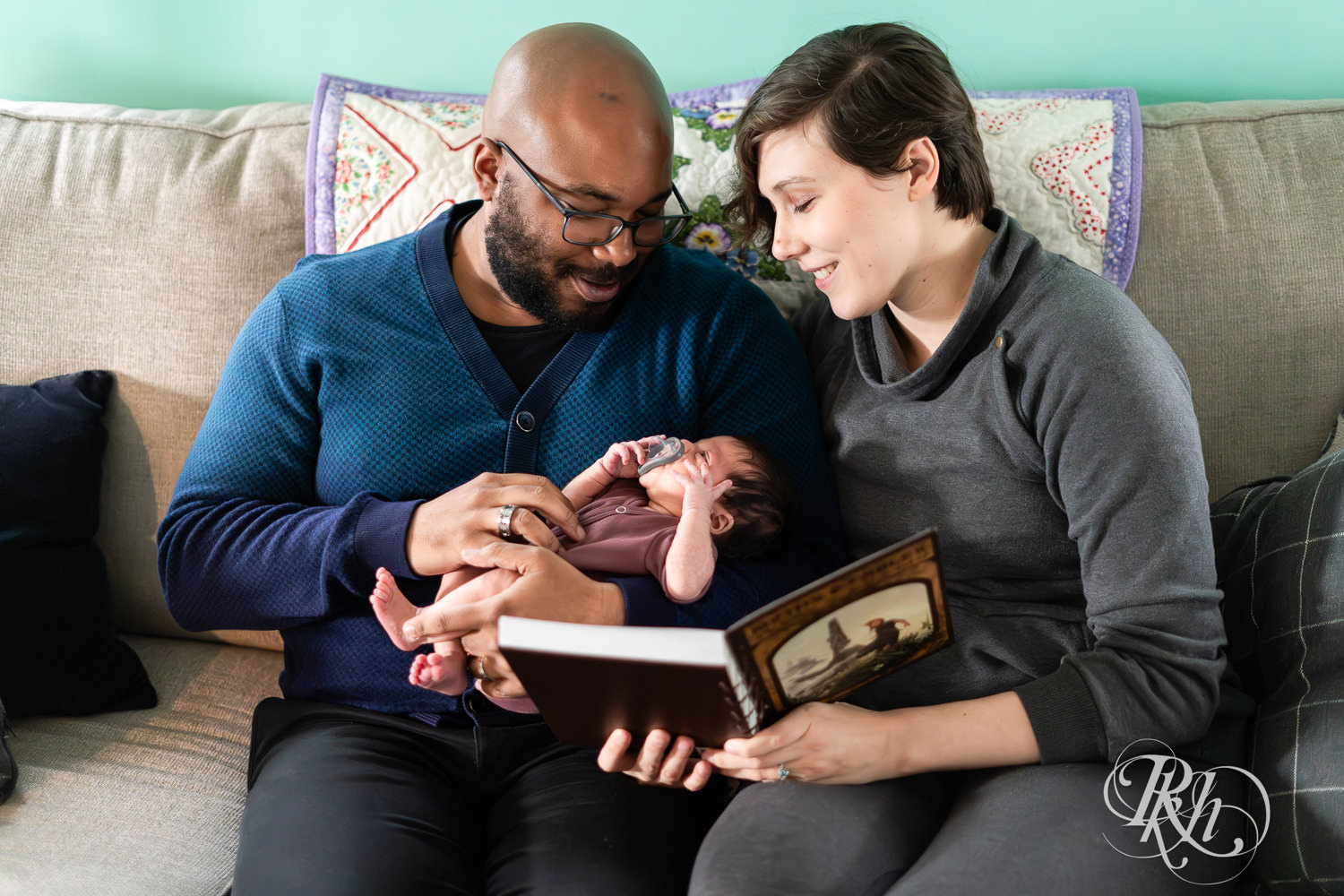 Black man and woman read to their newborn baby on the couch at home in Saint Paul, Minnesota.